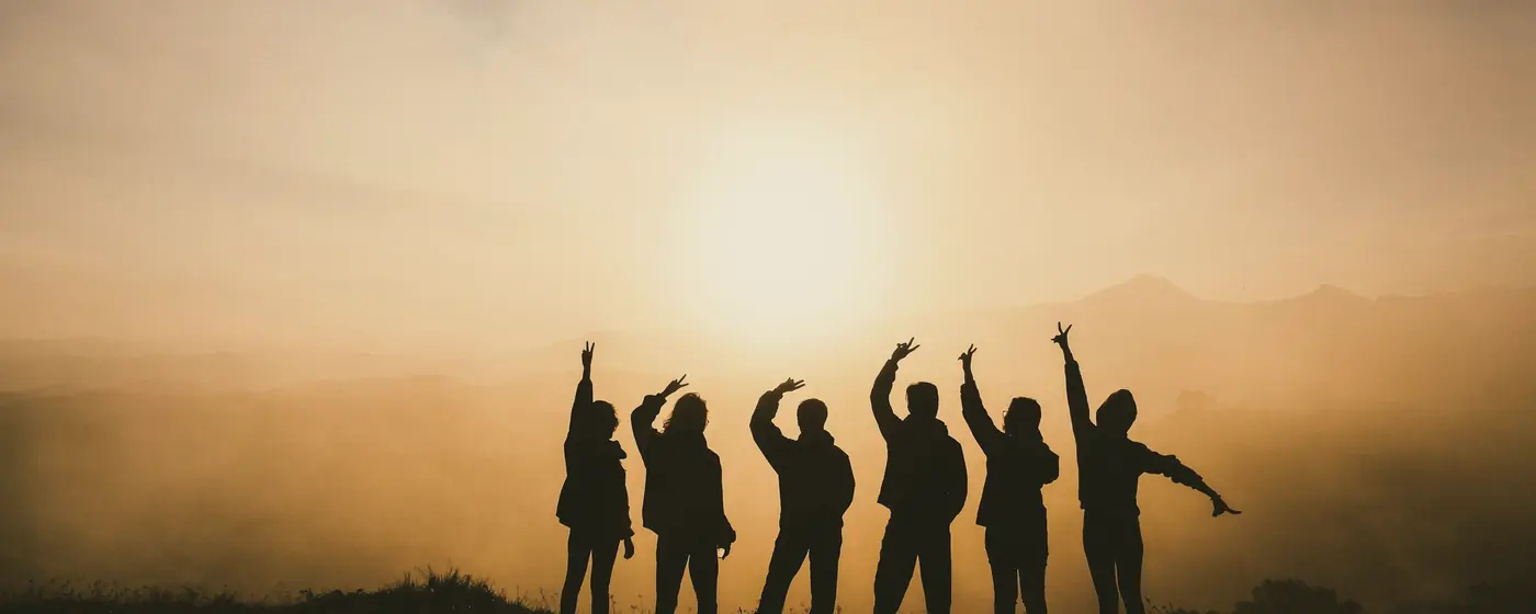 Friends silhouetted against a golden sunset, arms raised