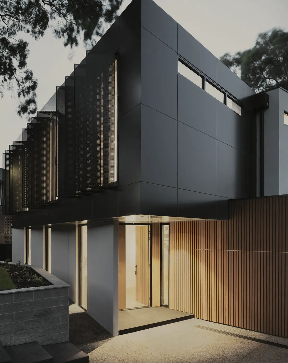 Dark contemporary façade with a warmly lit entrance at dusk