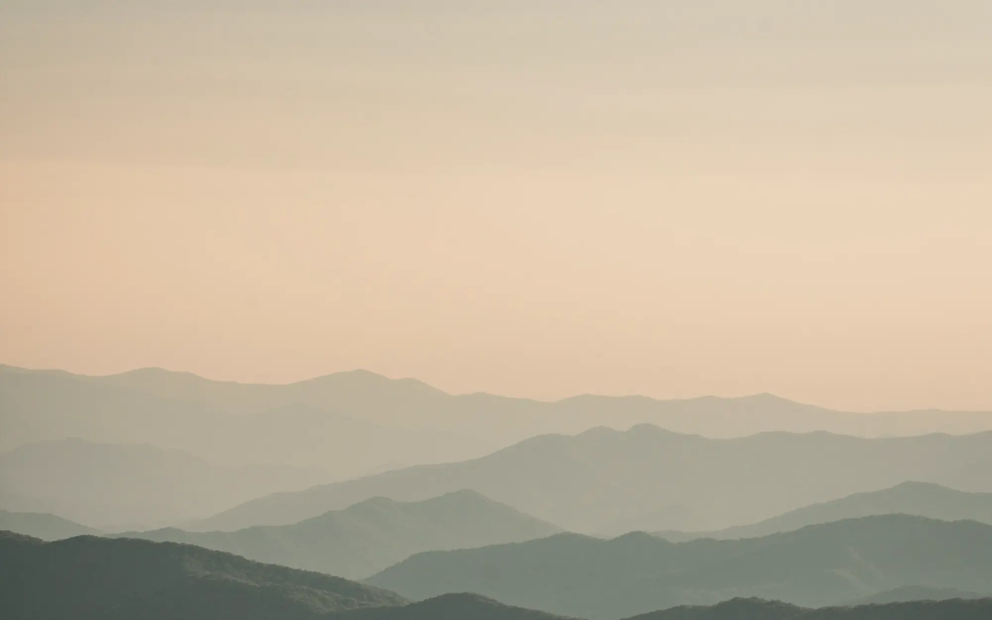 Layered mountain ridges fading into a warm evening haze